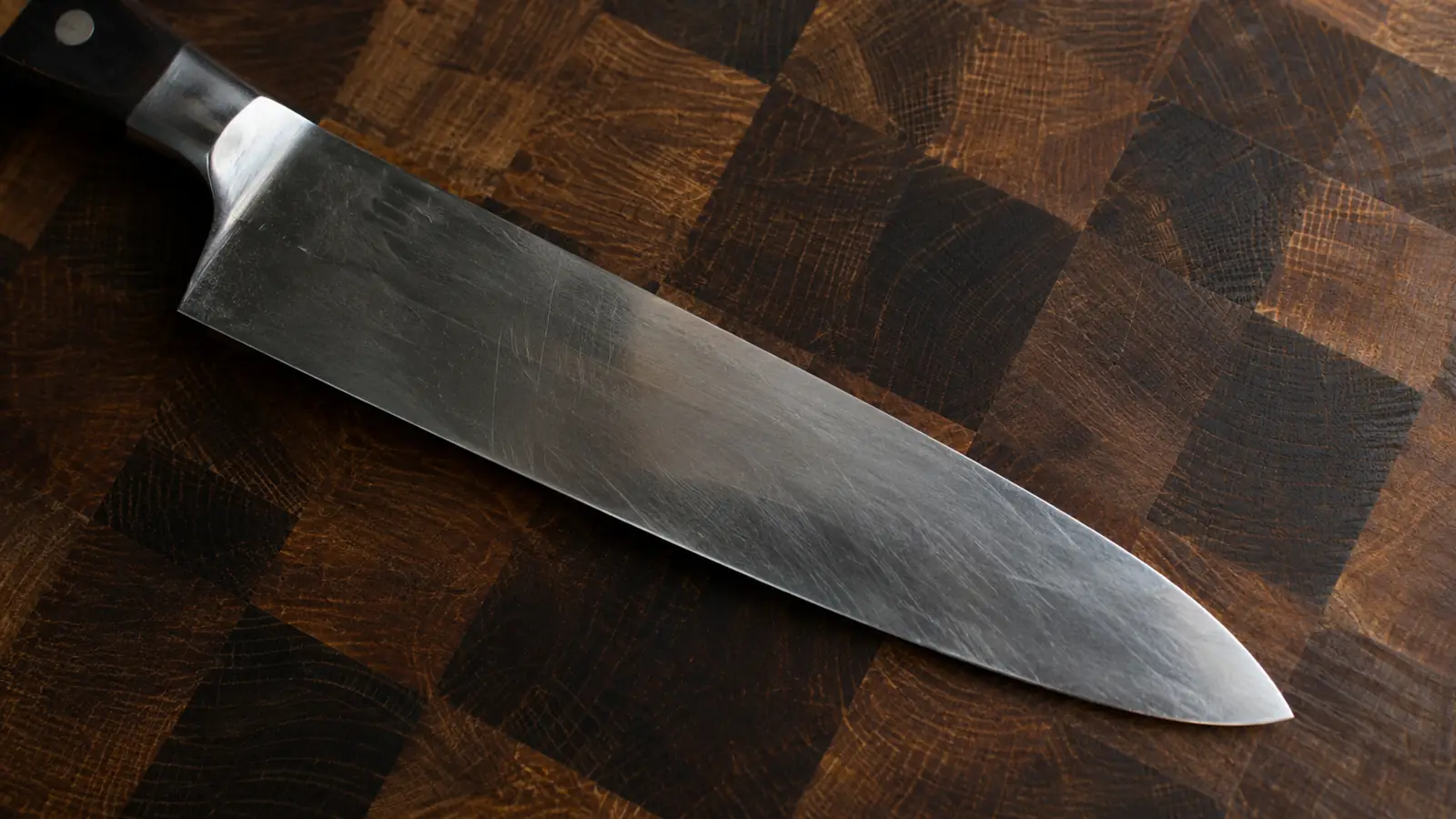 Close view of a knife edge resting in the checkerboard face of an end-grain board showing the wood fibers standing upright